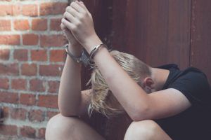 blonde teen wearing handcuffs by a brick wall | helping your child after an arrest
