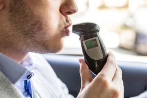 man-blowing-into-breathalyzer-while-sitting-in-front-of-car-sm