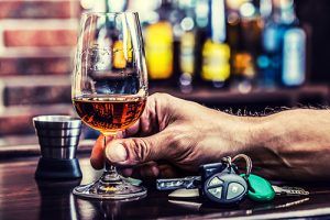 man holding glass of liquor on bar next to dram and keys | Colorado is the 21st Worst State for DUI 