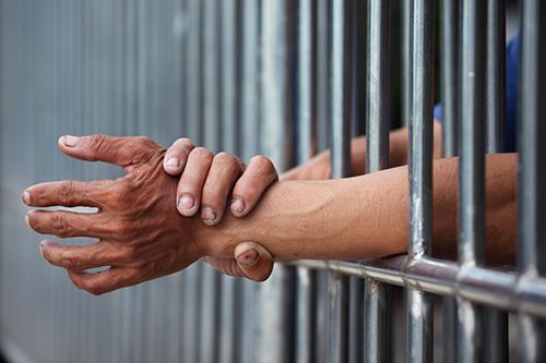 man rubbing his wrist arms between jail cell bars | Long-Term Consequences of a Criminal Conviction